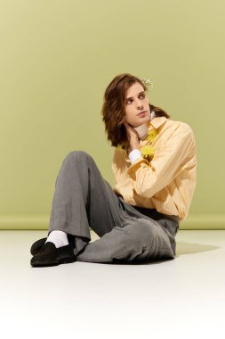 Tarz sahibi genç bir adam pastel bir zemine yaslanır, cazibesi ve modası geçer..