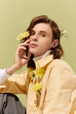 Şık bir genç adam yeşil bir zemine karşı düşünceli ve renkli çiçeklerle poz verir..