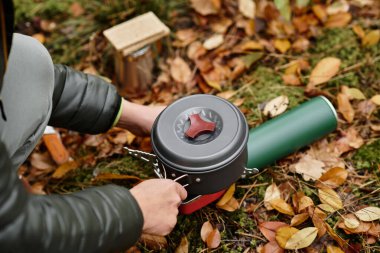 Düşen yaprakların arasında, yaşlı bir kadın ormanda taşınabilir bir sobanın üzerinde yemek hazırlıyor..