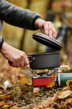 Yaşlı bir kadın canlı bir ormanda yürüyüş yapıyor, yaprakların arasında sobanın üstünde yemek pişiriyor..