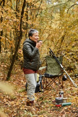 Yaşlı kadın ormanda sakin bir yürüyüş sırasında doğanın tadını çıkarırken sıcak bir içecek yudumluyor..