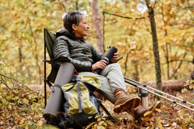 Yaşlı kadın, renkli sonbahar yaprakları ve yükselen ağaçların arasında yürüyüş yaparken huzur dolu bir mola veriyor..