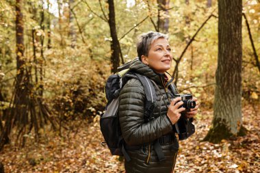 Kıdemli bir kadın, sonbaharda canlı bir ormanda yürürken doğaya hayran olur..