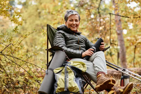 Yaşlı kadın, renkli sonbahar yapraklarıyla çevrili uzun bir yürüyüşten sonra ormanda dinleniyor..