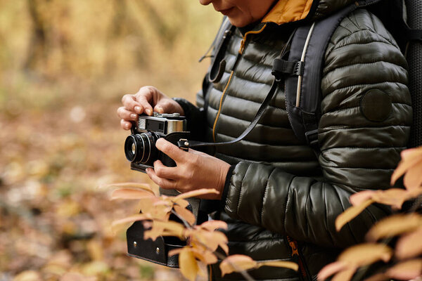 Старшая женщина исследует тихий лес, делая увлекательные фотографии природы с помощью фотоаппарата.