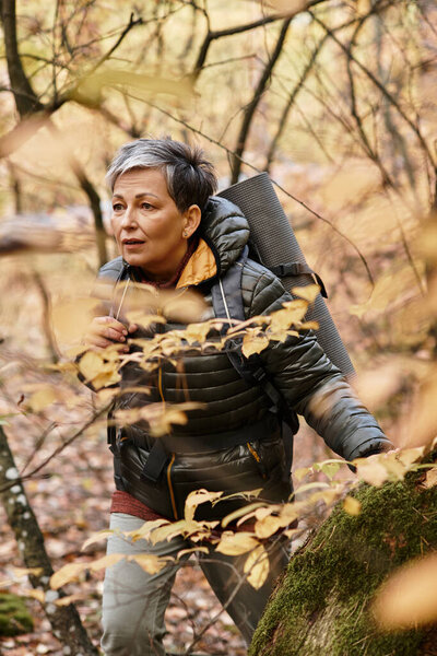 A senior woman joyfully hikes through a forest filled with golden leaves, embracing natures beauty.