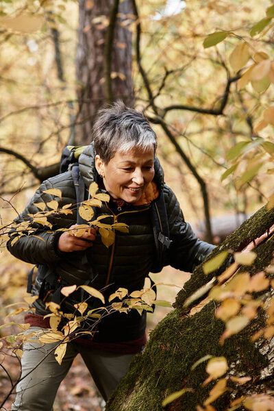 A senior woman explores the lush forest, surrounded by colorful autumn foliage and vibrant nature.