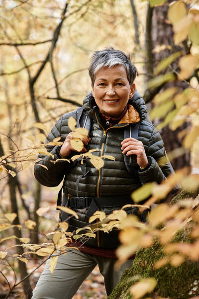 A senior woman hikes through a vibrant autumn forest filled with colorful leaves.