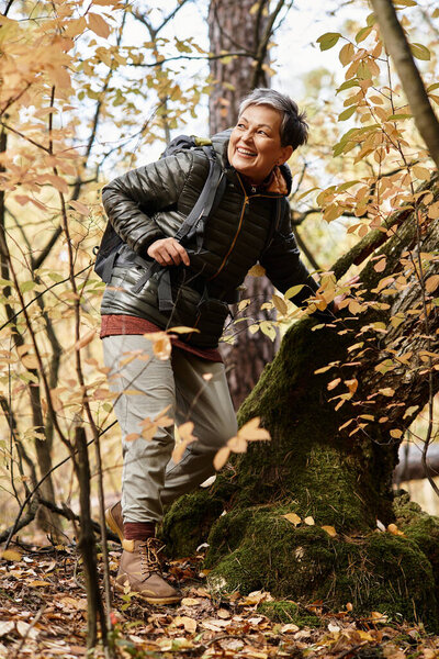 Senior woman enjoys a delightful hike through a colorful forest filled with autumn leaves.