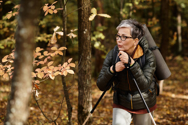 A senior woman explores a vibrant forest, taking in the beauty of autumn foliage while hiking.