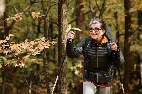 Senior woman enjoys a refreshing hike through the vibrant autumn forest surrounded by trees.