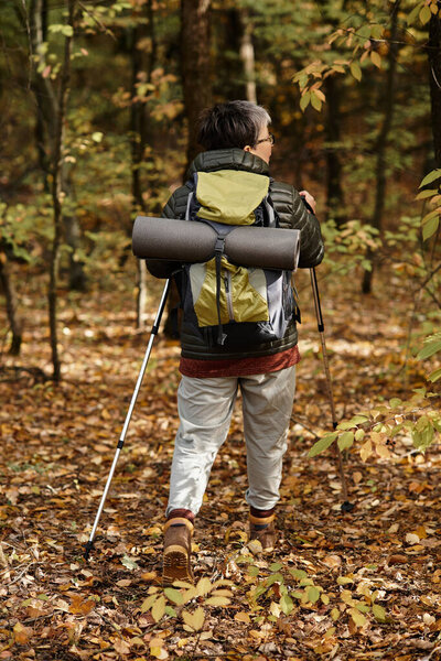 A senior woman hikes thoughtfully on a serene forest trail lined with vibrant autumn leaves.