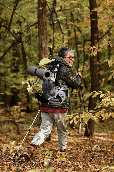 Joyful senior woman hiking in a dense forest with striking autumn colors and scenic trails.