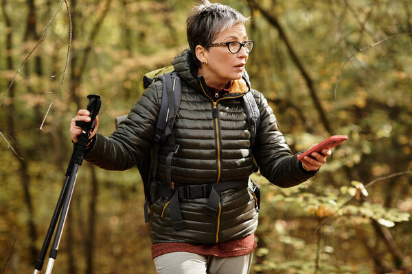Senior woman enjoys a peaceful hike in a lush forest, engaging with her smartphone for navigation.