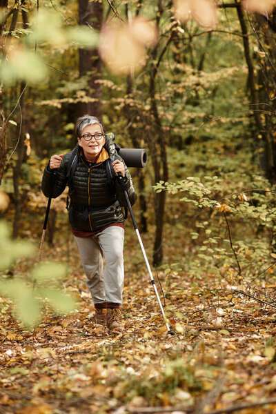 Senior woman enjoys hiking in a lively forest surrounded by the rich colors of autumn foliage.