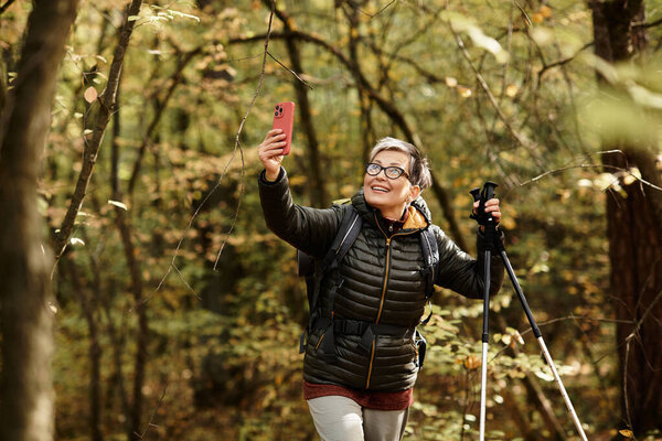 A cheerful senior woman captures a moment during her hike through a beautiful, lush forest.