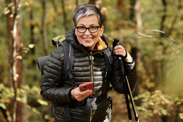 A senior woman enjoys her hiking adventure in a lush forest filled with autumn colors.