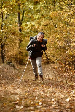 Kıdemli kadın, sonbahar yapraklarıyla çevrili manzaralı bir patikada yürürken doğayı kucaklıyor..