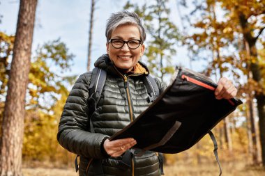 Güzel bir orman ortamında, yaşlı bir kadın yürüyüş yaparken sırt çantasını inceler..