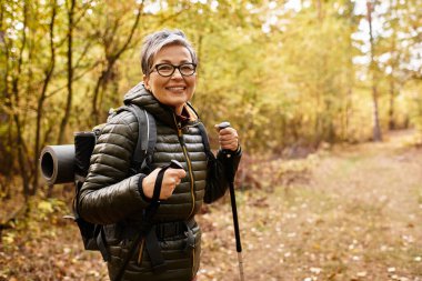 Kıdemli kadın, sonbahar renkleriyle çevrili canlı ormanda ferahlatıcı bir yürüyüşün tadını çıkarıyor..