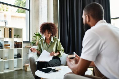 Çağdaş bir stüdyoda, bir kadın notlar alırken, gülümserken bir görüşmeye katılır..