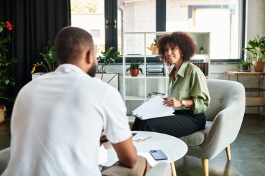 Genç bir kadın bitkilerle dolu çağdaş bir stüdyoda adayla röportaj yapıyor..