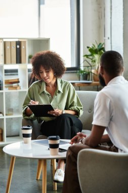 Genç bir kadın, şık bir stüdyoda potansiyel iş uygunluğunu tartışmak için bir erkek adayla röportaj yapıyor..