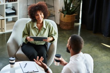 Genç bir kadın şık bir stüdyo ortamında adayla röportaj yaparken gülümsüyor..
