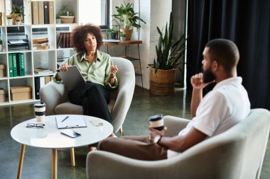 Genç bir kadın, gün içinde çağdaş bir stüdyo ortamında bir adamla röportaj yapıyor..
