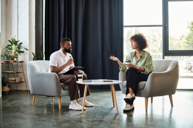 Genç bir adam ve kadın modern bir stüdyo ortamında mülakat sırasında sohbet ediyorlar..