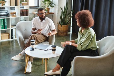 İki genç profesyonel, şık bir stüdyo ortamında iş fırsatlarını tartışıyor..