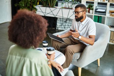 Genç bir adam, yeşillik dolu şık bir stüdyoda bir kadınla röportaj yapıyor..