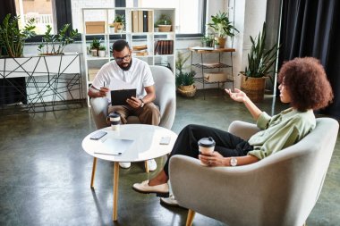 Genç bir kadın, modern bir stüdyoda otururken bir erkekle niteliklerini tartışıyor..