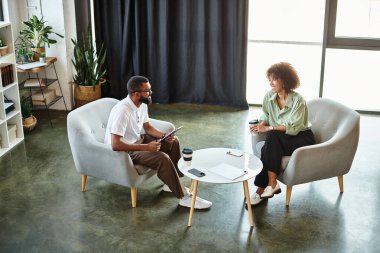 Genç bir adam ve kadın, modern bir stüdyo ortamında fikir alışverişinde bulundular..