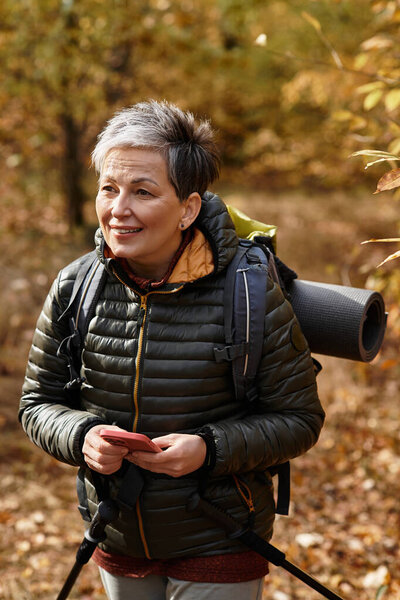 Amidst the golden leaves, a senior woman is happily exploring forest trails with her hiking gear.