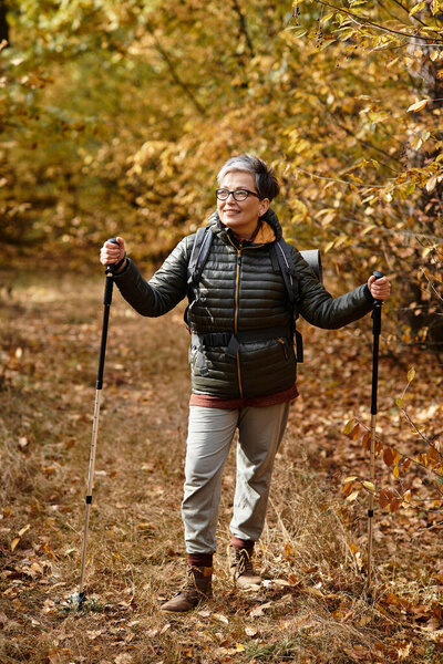 A senior woman enjoys a refreshing hike through vibrant autumn foliage with trekking poles.