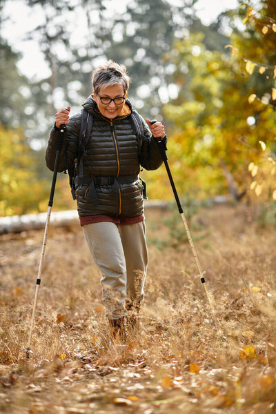 Senior woman joyfully explores a forest trail during autumn, embracing natures beauty.