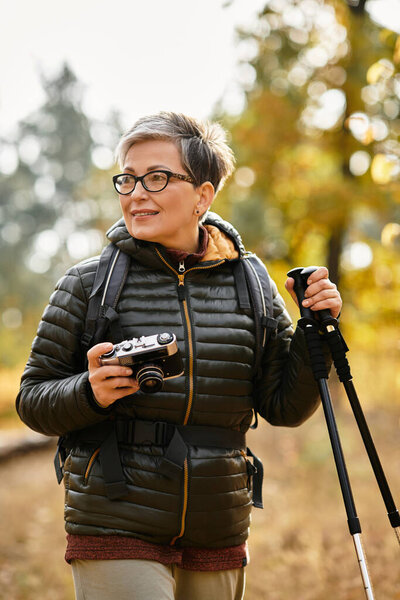 A senior woman smiles while hiking in a vibrant forest, capturing natures beauty.