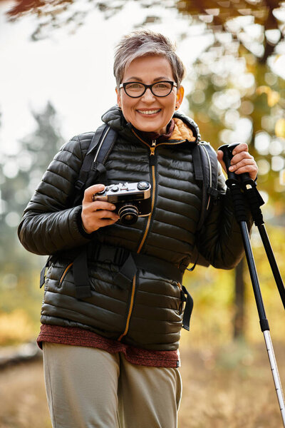 A senior woman smiles and documents her journey through a peaceful forest.