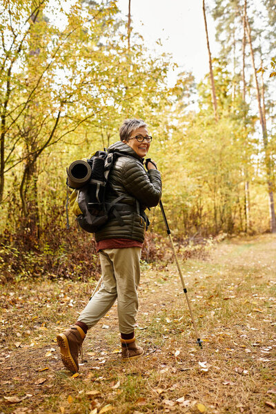 Senior woman enjoys a peaceful hike in the woods, surrounded by autumn foliage and natures beauty.