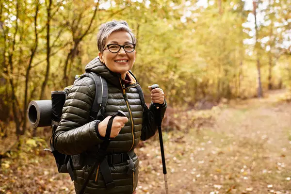 Kıdemli kadın, sonbahar renkleriyle çevrili canlı ormanda ferahlatıcı bir yürüyüşün tadını çıkarıyor..