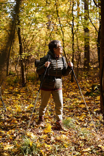Senior woman enjoys a peaceful hike surrounded by colorful autumn foliage in the forest.