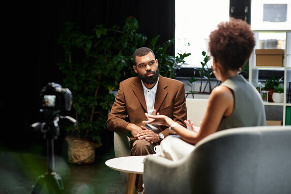 Молодая женщина берёт интервью у мужчины в современной студии, оба занимаются беседой.