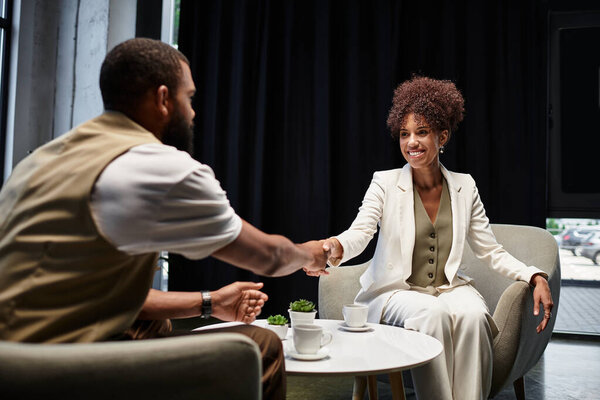 Young man and woman shake hands, exchanging smiles in a stylish studio during the interview.