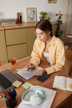 Yaratıcı projelerle meşgul olan genç bir kadın, evde bir fincan çay içerken notlar alıyor..