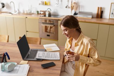 Sıcak ve davetkar bir mutfakta genç bir kadın içkisini yudumlarken ve çalışırken gülümser..