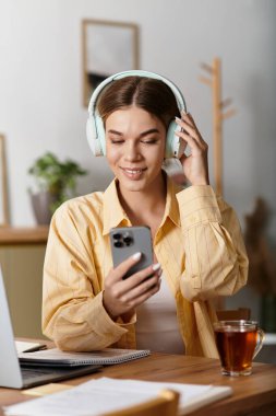 Genç bir kadın evde rahatça oturup kulaklıklarıyla müzik dinlerken gülümsüyor..