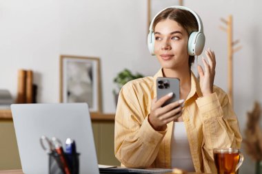 Evde dinlenen genç bir kadın, telefonuyla kulaklıkla müzik dinliyor..