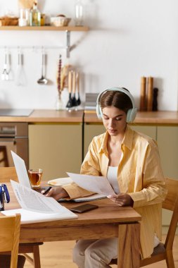 Genç bir kadın sıcak bir mutfakta belgeleri incelerken çaydan hoşlanır..
