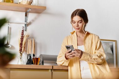 Rahat bir ev ortamında genç bir kadın, içki içerken akıllı telefonuyla meşgul..